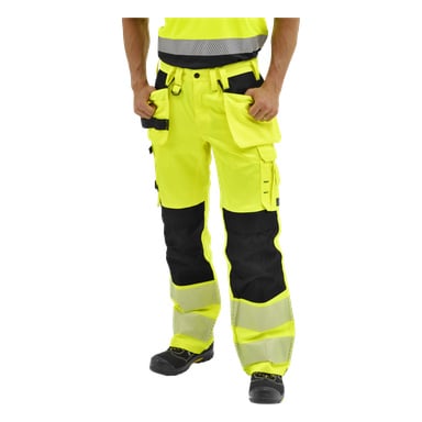 Die Person steht mit den Händen in den Taschen, trägt gelbe und schwarze Bluewear Hi-Vis-Hosen mit reflektierenden Bändern und schwarze Arbeitsschuhe.
