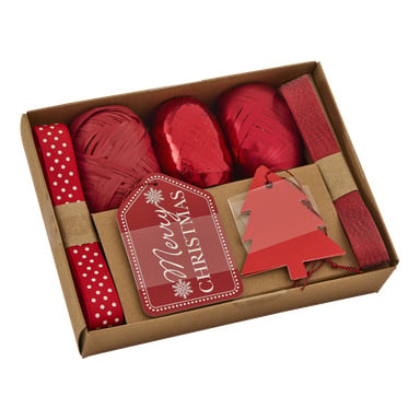 En box med presentinslagningsmaterial med jultema, inklusive rött band, två spolar rött garn, en rulle röd raffia, en Merry Christmas-tagg och en röd trädformad tagg.