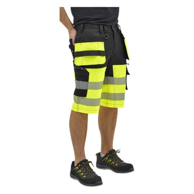 Underkroppen på en person i svarta och gula högtidsshorts med reflekterande band, flera fickor och svarta arbetsskor.
