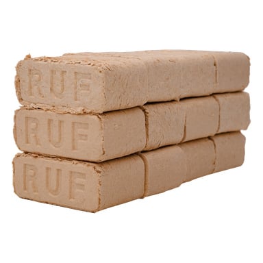 Tre staplar rektangulära, komprimerade träbriketter från No är prydligt arrangerade. Varje stapel har tre tätt packade briketter med grova kanter och en enhetlig beige färg.