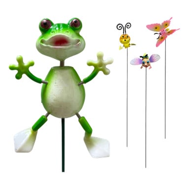 En grön och vit grodfigur med utsträckta armar från Hard Heads trädgårdsdekorationssamling står på en pinne, flankerad av tre trädgårdspålar i form av ett gult bi, en rosa fjäril och en insekt med blå vingar.