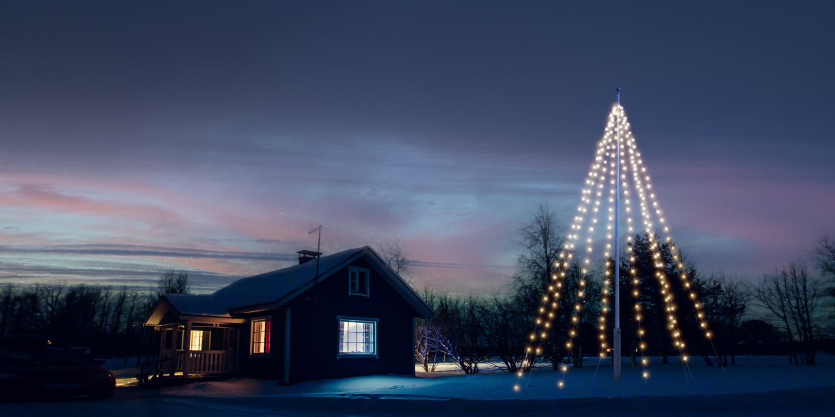 Bei Einbruch der Dämmerung leuchtet ein gemütliches Haus in verschneiter Umgebung. Daneben zeigen Masten Lichter in Form eines riesigen Weihnachtsbaums.