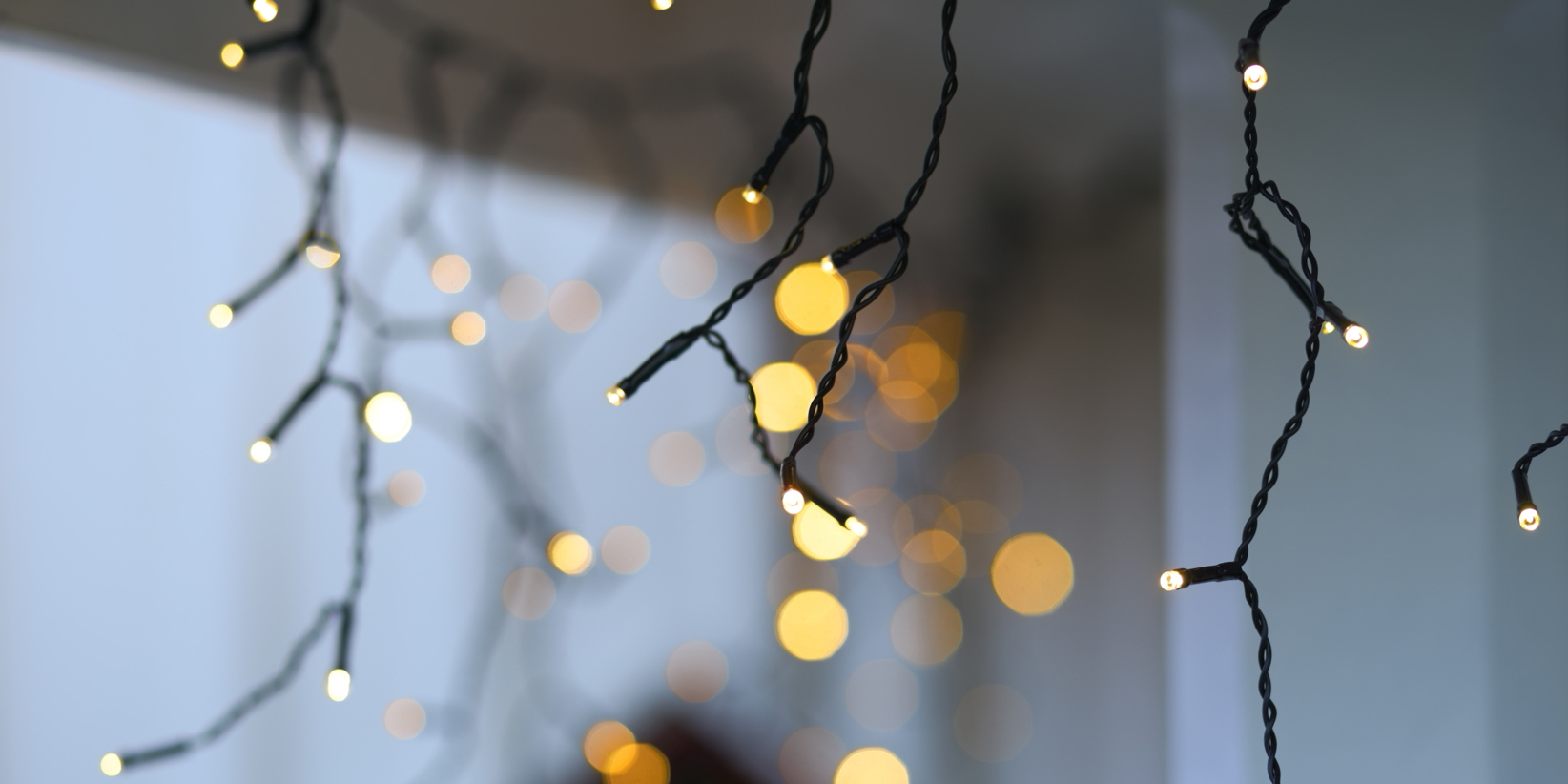 Nahaufnahme von weißen LED-Lichterketten, die hängen, verschwommenes gelbes Bokeh im Hintergrund mit einem sichtbaren Blick auf einen Fensterrahmen.