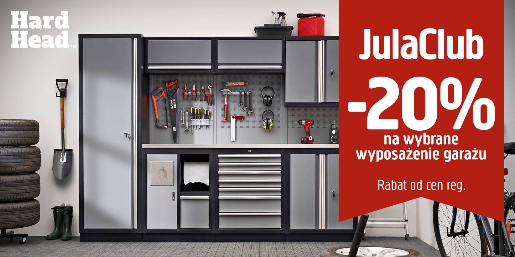 Nowoczesny garaż z uporządkowanymi narzędziami i szafkami do przechowywania. Po prawej stronie widnieje czerwony baner z napisem: „JulaClub – 20% na wybrane wyposażenie garażu. Rabat od cen regulaminowych”. Na pierwszym planie widać cztery opony i fragment roweru.