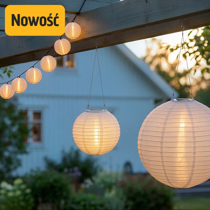 Dwa duże i kilka małych białych papierowych lampionów świeci na zewnątrz o zmierzchu. Żółta etykieta Nowość pojawia się nad domem i zielenią.