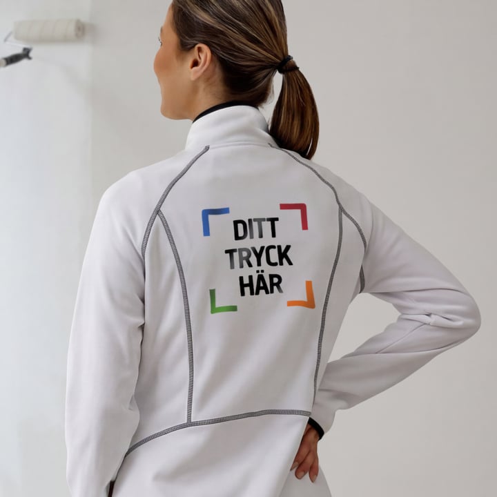 En person i vit jacka med "DITT TRYCK HÄR" och fyra färgade hörnfästen på ryggen, sedd bakifrån inomhus.