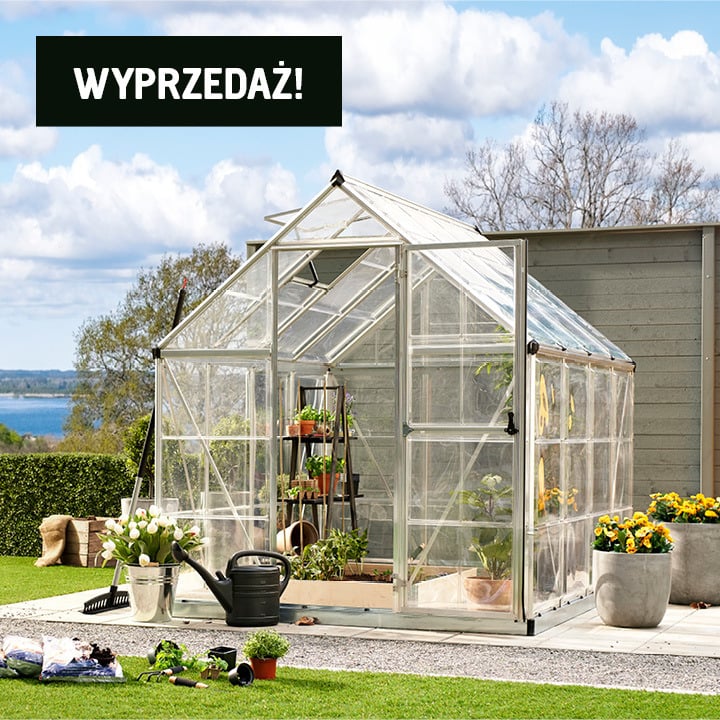 Szklarnia o metalowej ramie stoi na patio z roślinami w środku i narzędziami w pobliżu. W lewym górnym rogu widnieje napis "WYPRZEDAŻ!".