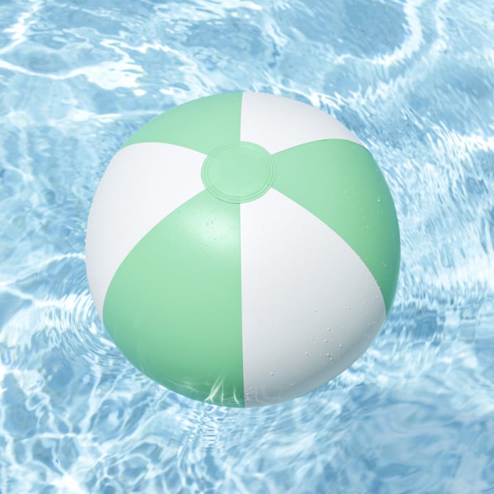 En grønn og hvitstripet strandball driver oppå et klart blått basseng, med krusende vann og refleksjoner rundt.